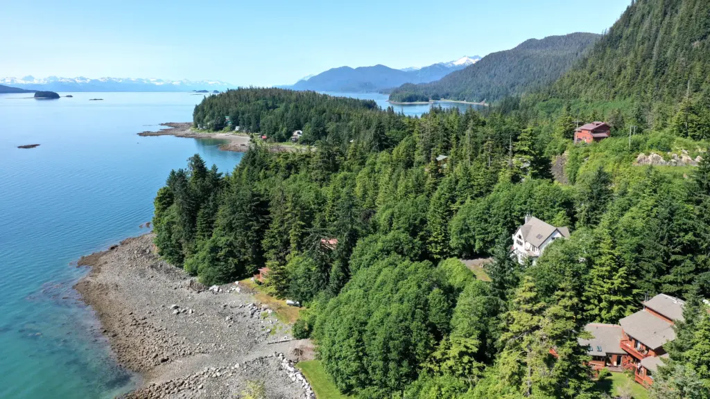 A forested coastline with small islands and distant mountain ranges across calm water