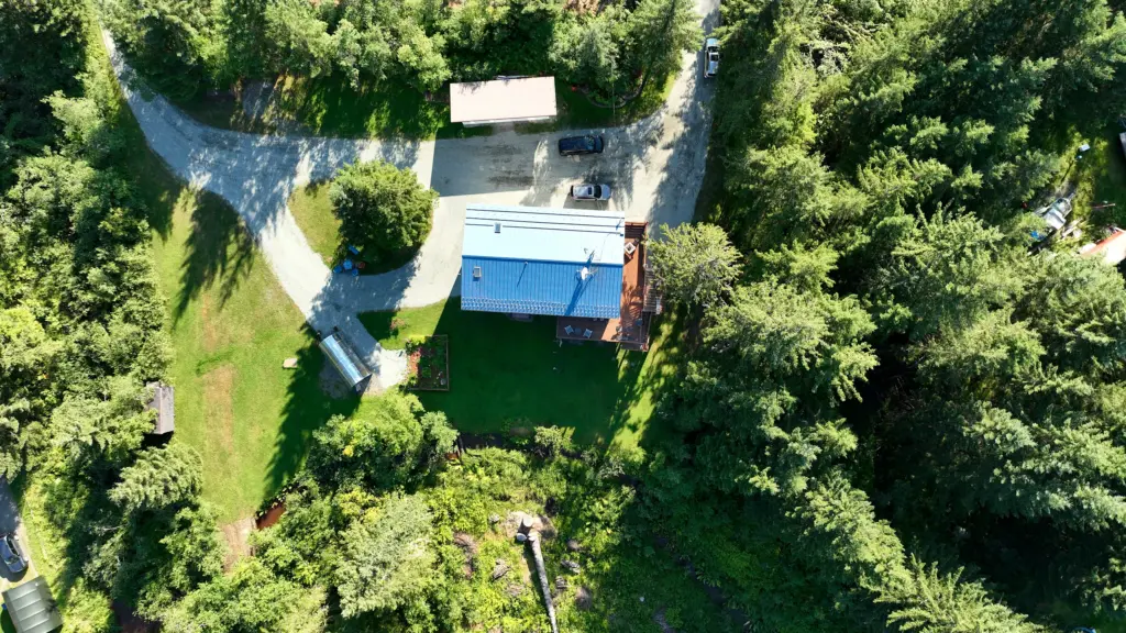 Top-down view of a home, gravel drive, garden and greenhouse surrounded by forest