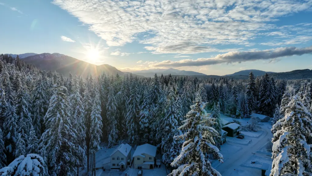 The sun rising over snowy forest, mountains and a quiet neighborhood under a mackerel sky