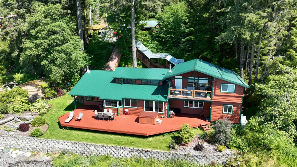 A cedar home with a green metal roof, large red deck and landscaped yard beside the beach