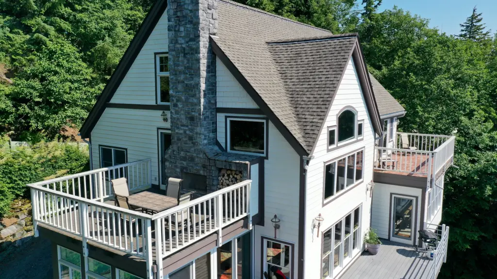 A home's deck and stone chimney overlooking forest, calm water and islands