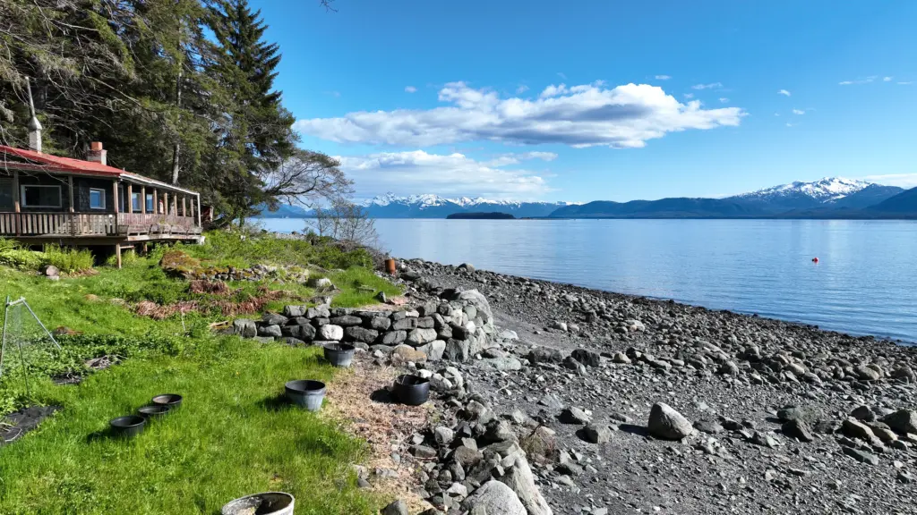 A beachfront cabin with rock walls looking out over calm water toward snowy mountains