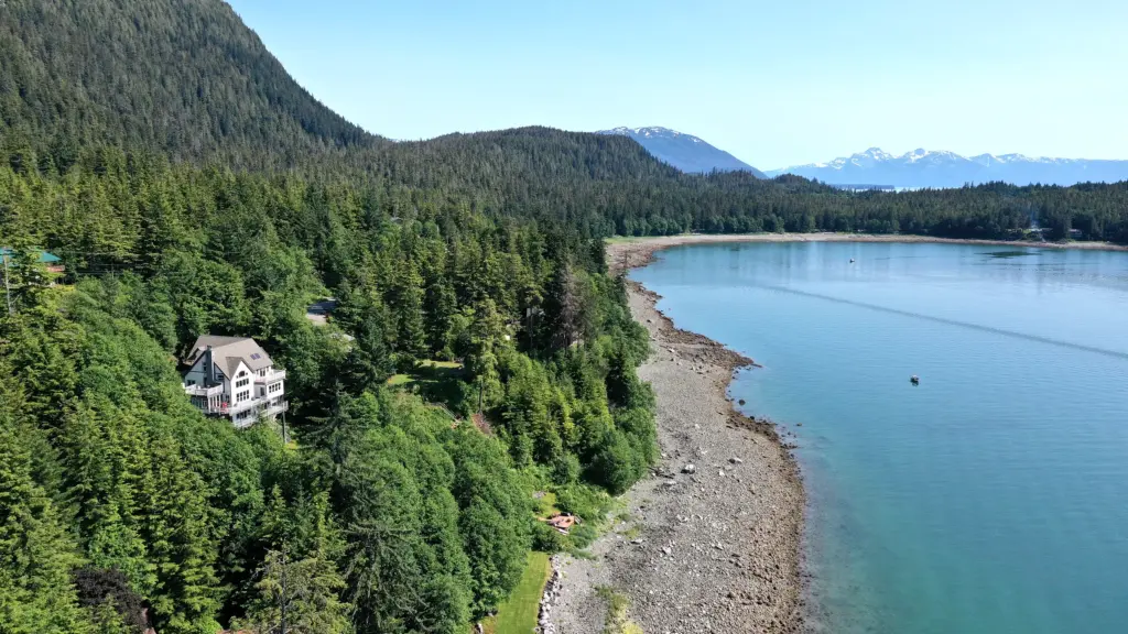 A long gravel beach curving along a turquoise inlet below forested hills
