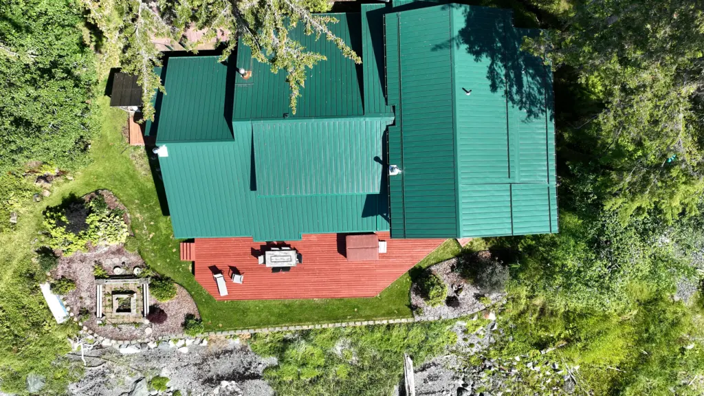 Top-down view of a home with a green metal roof, red deck and firepit near the beach