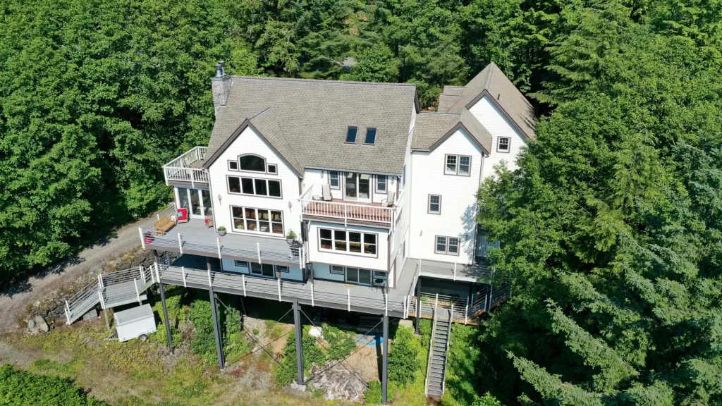 A tall white home with a stacked deck rising above a green forest