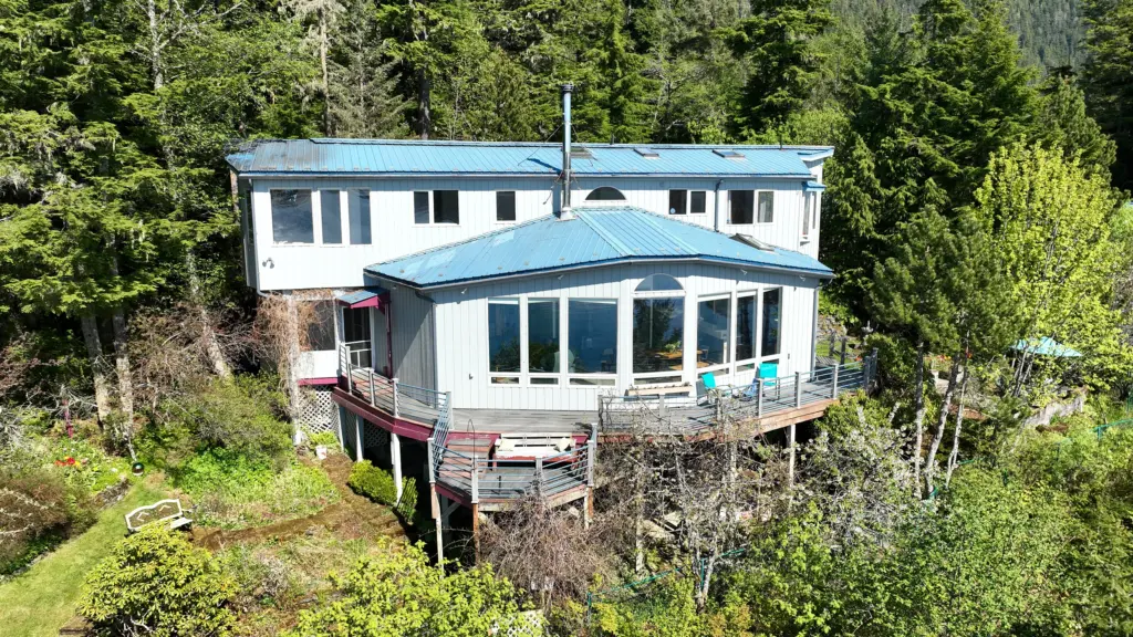 A large white home with wraparound windows and a deck on a lush hillside