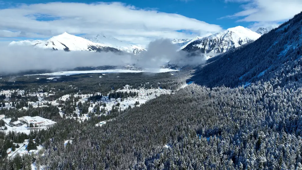 Snowy peaks with clouds above a valley of snow-covered forest and homes
