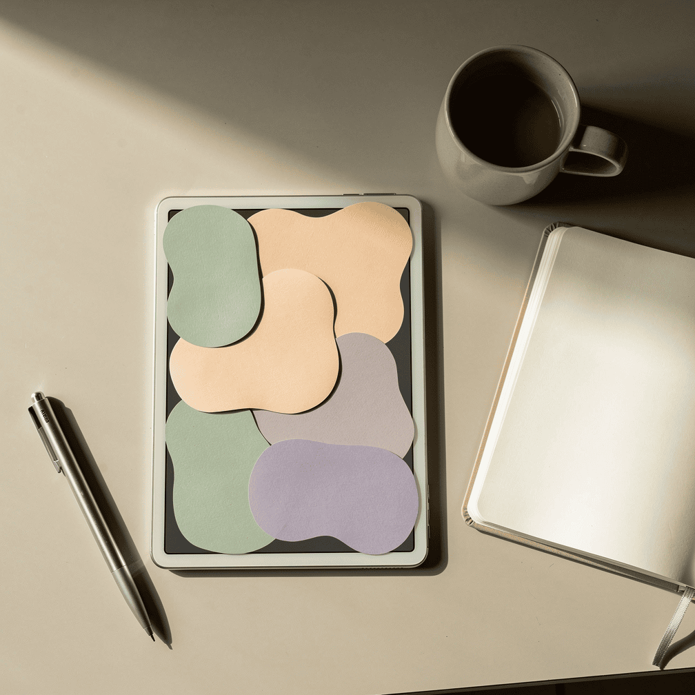 Designer's desk with pastel organic blob shapes arranged on a tablet and sketchbook